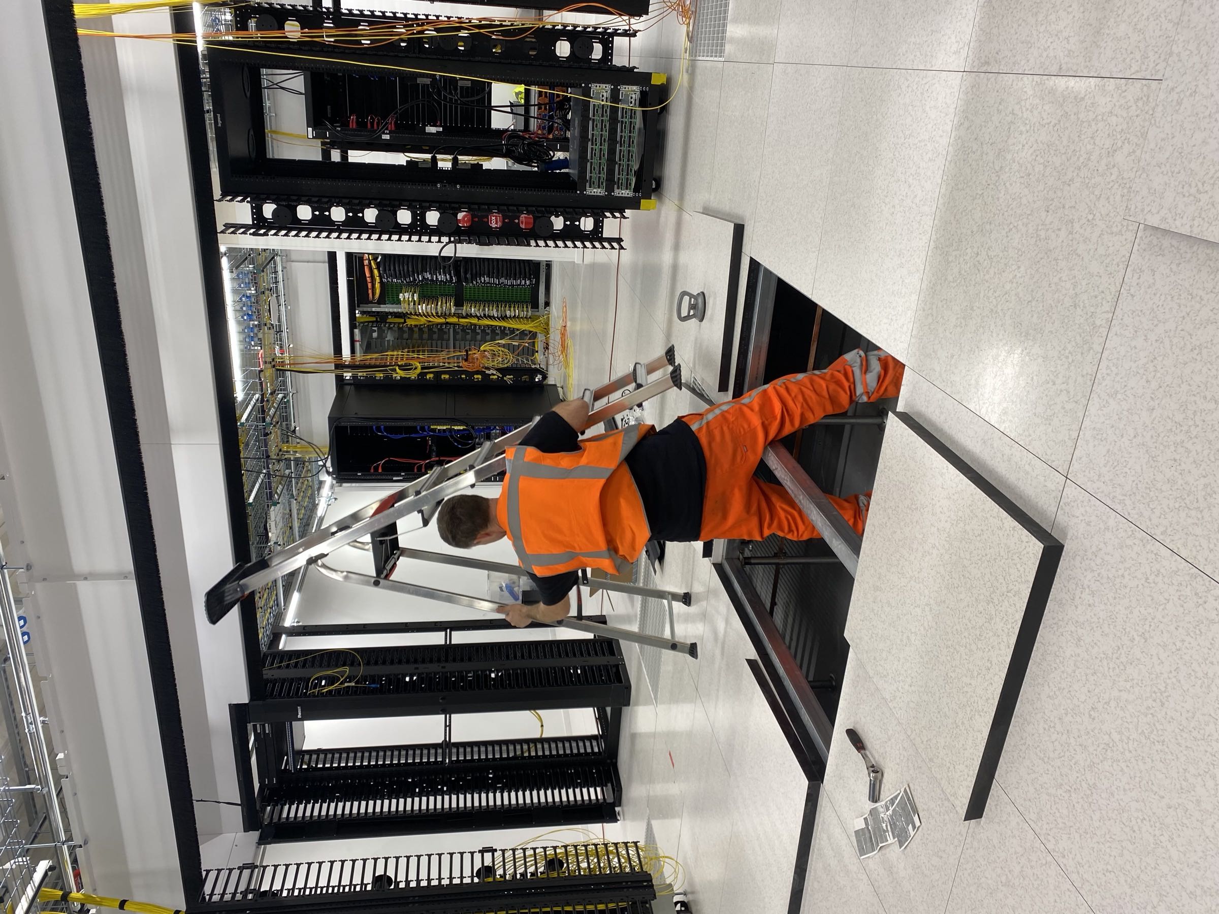 Anomalie monteur in datacenter op ladder bij serverkasten met open computervloer en zichtbare kabelinfrastructuur eronder