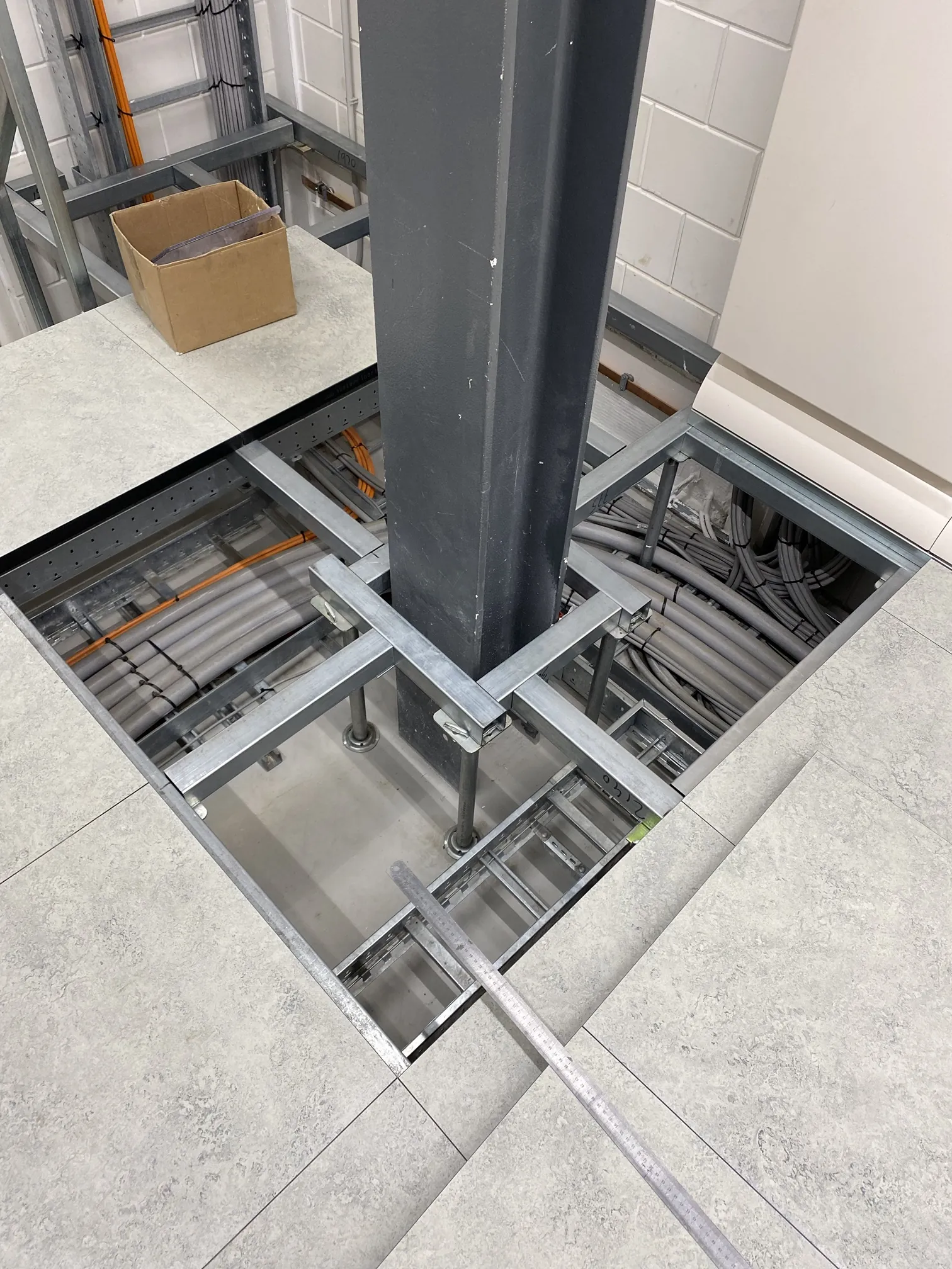 Geöffneter Systemboden im Rechenzentrum: Stahlprofile und Stützen rund um eine Säule, mit Kabeltrassen darunter, von Anomalie