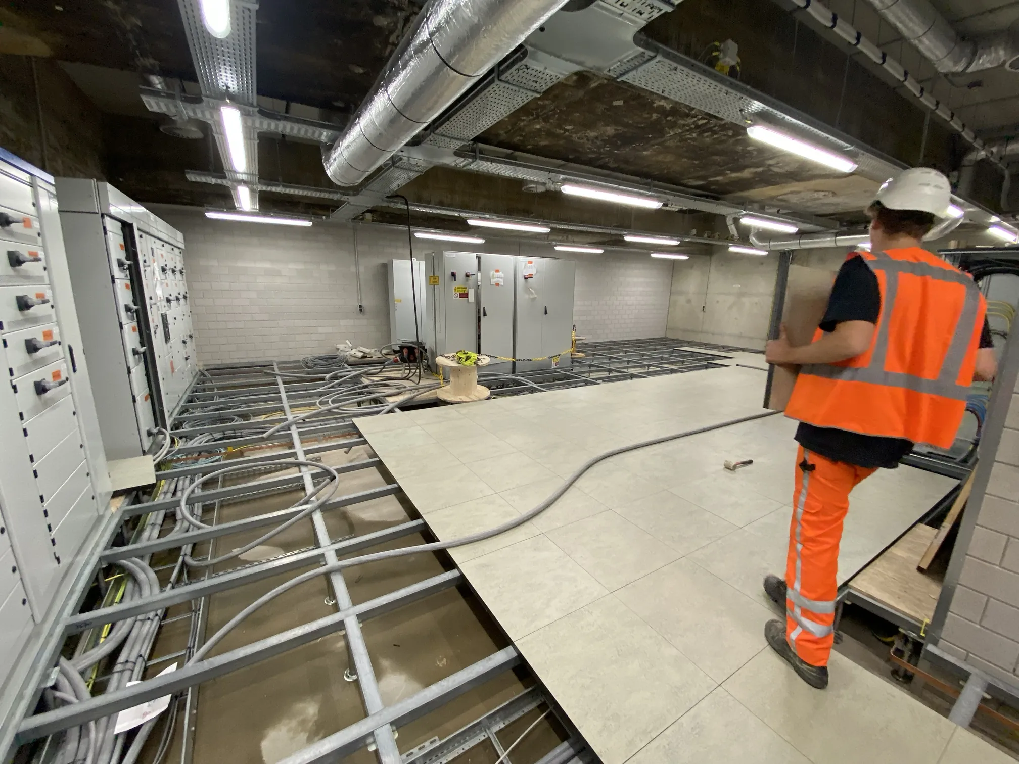 Montage van een systeemvloer met stalen draagconstructie in een regelstation, met schakelkasten en kabels onder de vloer, door Anomalie