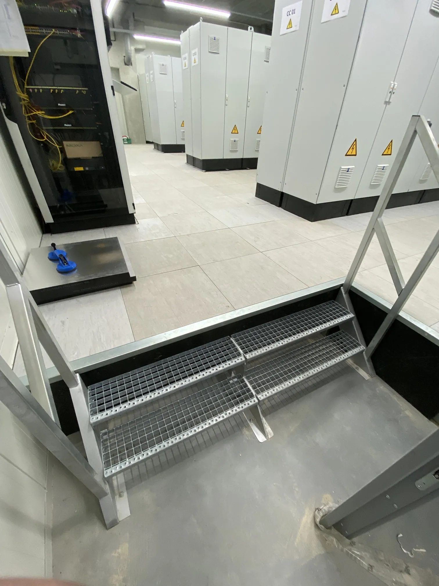 System floor in a technical room with switchgear cabinets and a custom steel staircase by Anomalie